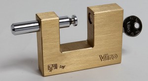     Un cadenas pour rideaux avec système d'ouverture à déclic, dans lequel l'axe de verrouillage est éjecté par un ressort du côté opposé à la clé.